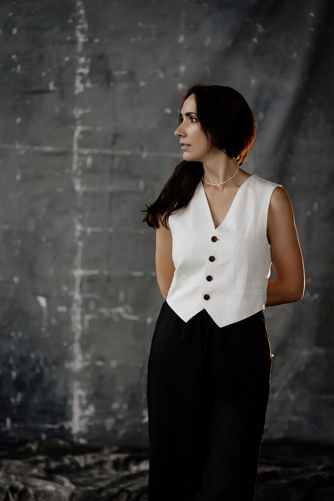 Stylish woman in a white vest and black trousers posing in front of a textured gray studio backdrop during a professional portrait photoshoot